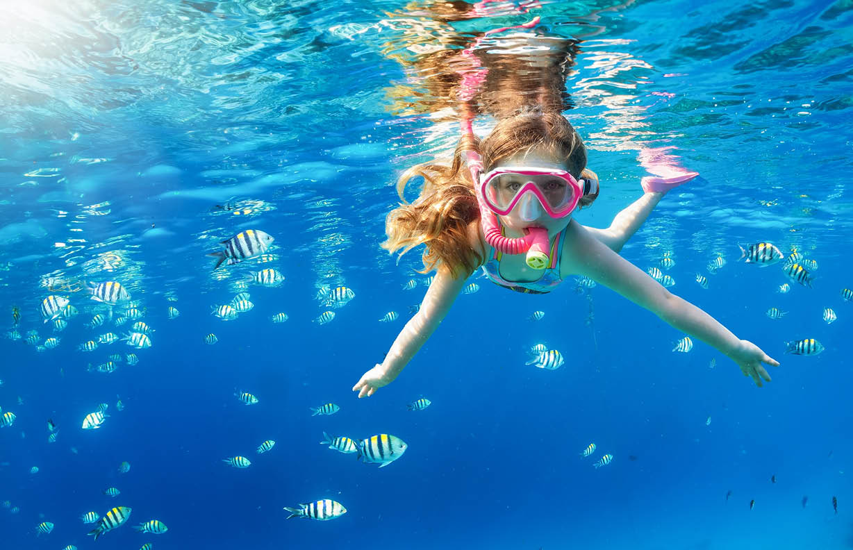A little girl with mask and snorkel enjoys the underwater life of the tropical ocean wth colorful fishes in the Maldives