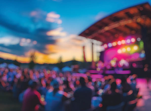 Blurred background of vibrant atmosphere of a summer concert held in an outdoor arena, featuring a lively audience cheering as the sun sets, creating a memorable experience.