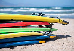 Set of different color surf boards in a stack by ocean. Surf boards for rent on sandy beach. Soft toned photo.