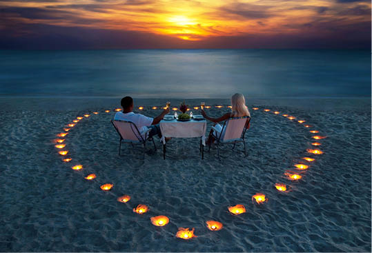A young couple share a romantic dinner with candles heart on the sea sand beach