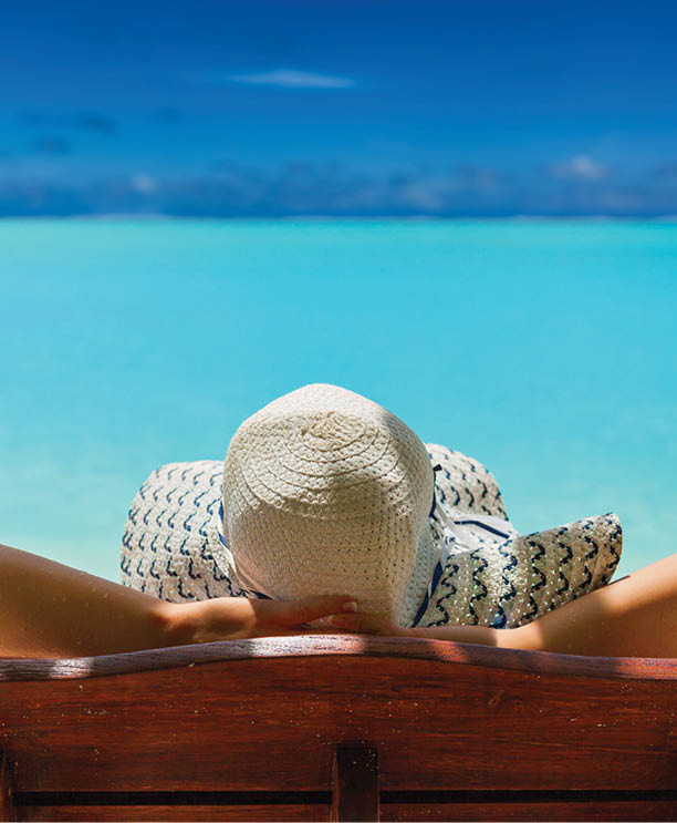 girl lays on a chaise lounge in the back on the banks of the turquoise Caribbean sea on Bahamian Maldivian Hawaiian beaches