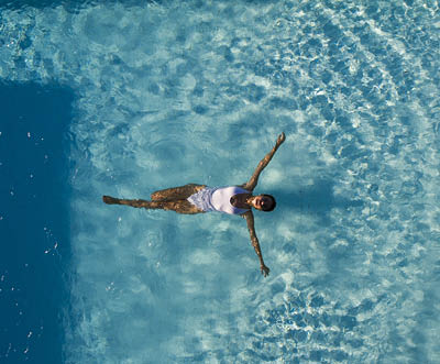 Top view aerial photo from flying drone of a seductive sexy model in white swimwear is enjoying relax in hotel pool during her summer weekend. Amazing fashion woman in bikini having luxury spa rest