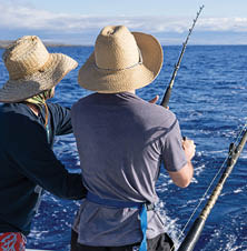 Two men fishing on a boat. Fishing trip while on vacation. Deep blue water, nice sky. 