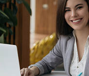 Portrait of beautiful confident businesswoman using laptop computer taking notes working online in office. Smiling student studying looking at camera sitting modern library, education concept