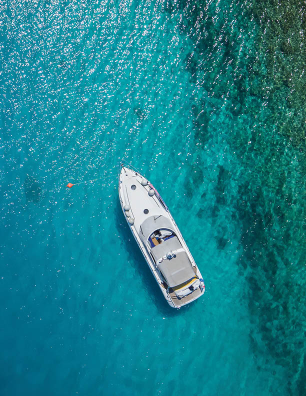 Luxury small yacht anchoring in shallow water, aerial view. Active life style, water transportation and marine sport.