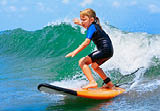 Happy baby girl - young surfer ride on surfboard with fun on sea waves. Active family lifestyle, kids outdoor water sport lessons and swimming activity in surf camp. Summer vacation with child.