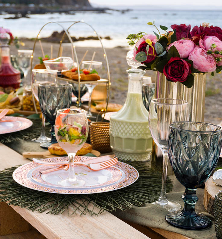 Picnic table on the beach in the style of boho, with assorted food and drinks