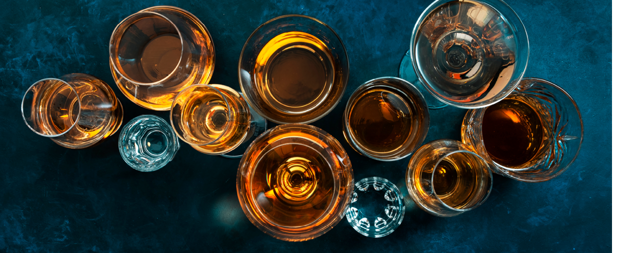 Strong alcohol drinks, hard liquors, spirits and distillates iset in glasses: cognac, scotch, whiskey and other. Blue background, top view 