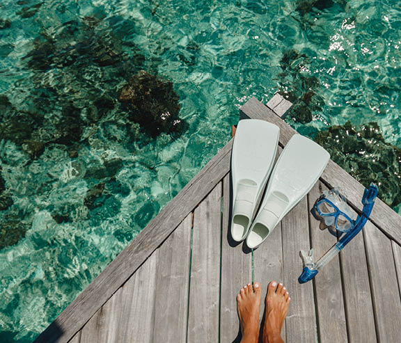 Beach vacation snorkel girl snorkeling with mask and fins. Equipment for snorkeling. Woman legs on wooden pier with snorkeling equipment