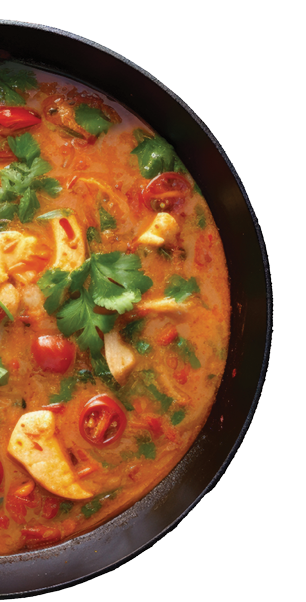 Coconut milk based fish stew with tomatoes red pepper coriander on dark wooden table