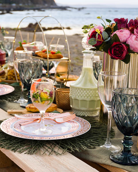 Picnic table on the beach in the style of boho, with assorted food and drinks
