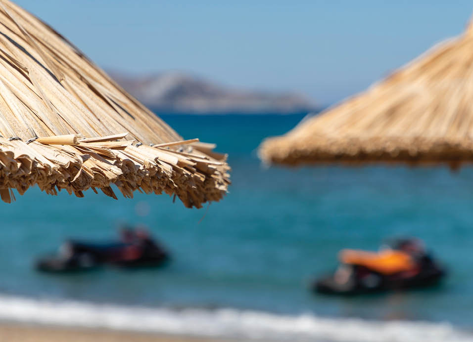 Beach umbrellas against the backdrop of mountains and jet skis. Active holidays on the Mediterranean coast