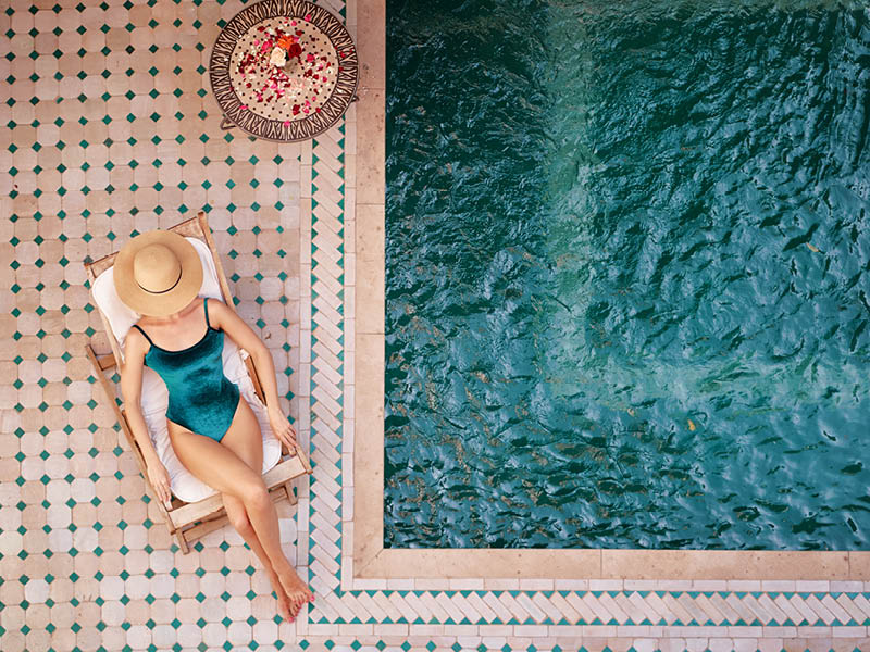 Enjoying suntan. Vacation concept. Top view of young woman on the sun lounger near the private swimming pool in beautiful moroccan backyard.