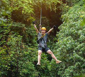 Freedom Man Tourist Wearing Casual Clothing On Zip Line Or Canopy Experience In Laos Rainforest, Asia