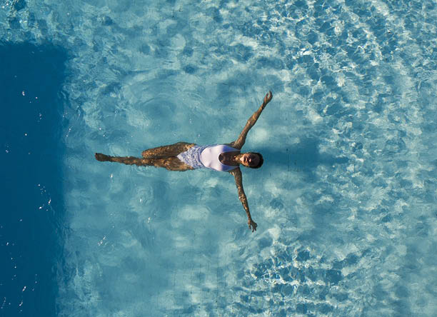 Top view aerial photo from flying drone of a seductive sexy model in white swimwear is enjoying relax in hotel pool during her summer weekend. Amazing fashion woman in bikini having luxury spa rest