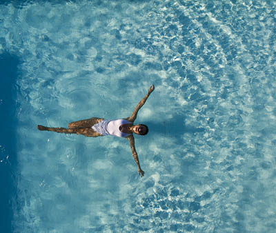 Top view aerial photo from flying drone of a seductive sexy model in white swimwear is enjoying relax in hotel pool during her summer weekend. Amazing fashion woman in bikini having luxury spa rest