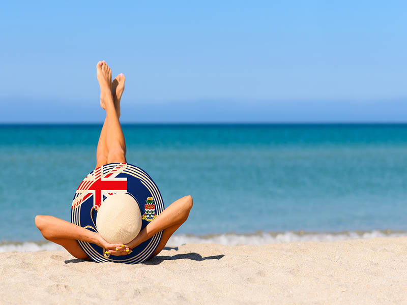 A slender tanned girl on the beach in a straw hat in the colors of the flag of the Cayman Islands. The concept of a perfect vacation in a resort in the Cayman Islands. Focus on the hat.