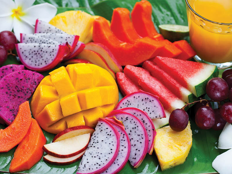 Tropical fruits assortment with fresh juice, palm leaf background. Top view. Close up