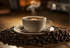 A white cup of steaming coffee placed on a saucer, surrounded by a pile of coffee beans