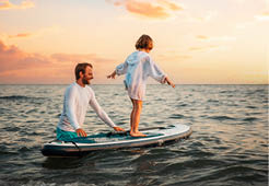 Surfing with sup board. Instructor teaches the pre-school girl to swim with a sup board. Sea and the sunset in the background. Summer vacations.