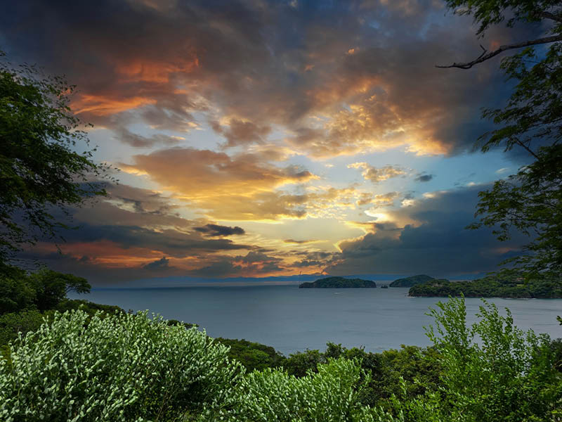 the blue waters of Culebra Bay, lush green trees and powerful clouds at sunset in Liberia Guanacaste Costa Rica