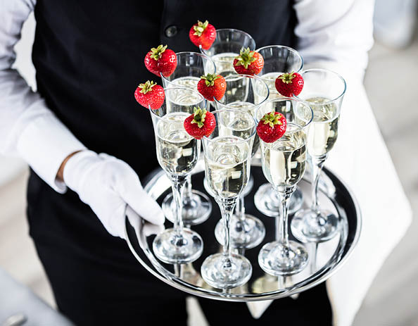 Waiter Standing With Champagne Glasses Next To Arranged Wedding Table