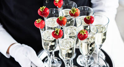 Waiter Standing With Champagne Glasses Next To Arranged Wedding Table