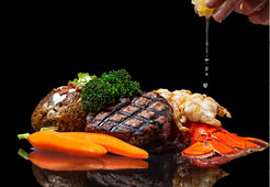 grilled lobster and filet mignon served with a loaded baked potato and vegetables isolated on a black background