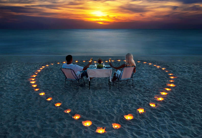 A young couple share a romantic dinner with candles heart on the sea sand beach