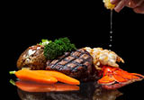 grilled lobster and filet mignon served with a loaded baked potato and vegetables isolated on a black background