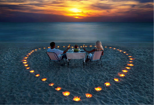 A young couple share a romantic dinner with candles heart on the sea sand beach