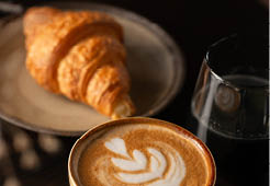 Cup of Cappuccino with beautiful cream latte art and a croissant on the side on a coffee shop table. Side view. Black Background.