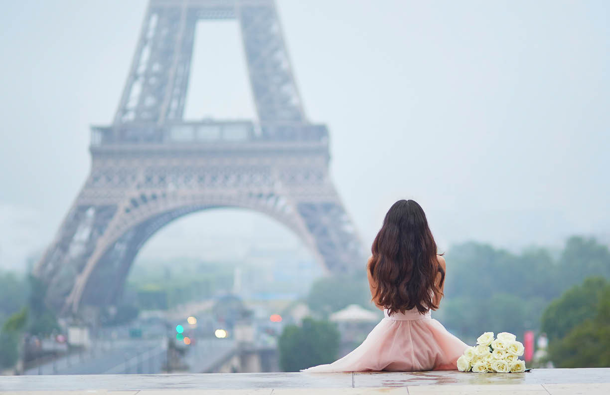 Elegant Parisian woman in pink tutu dress with white roses sitting near the Eiffel tower at Trocadero view point in Paris, France, back view