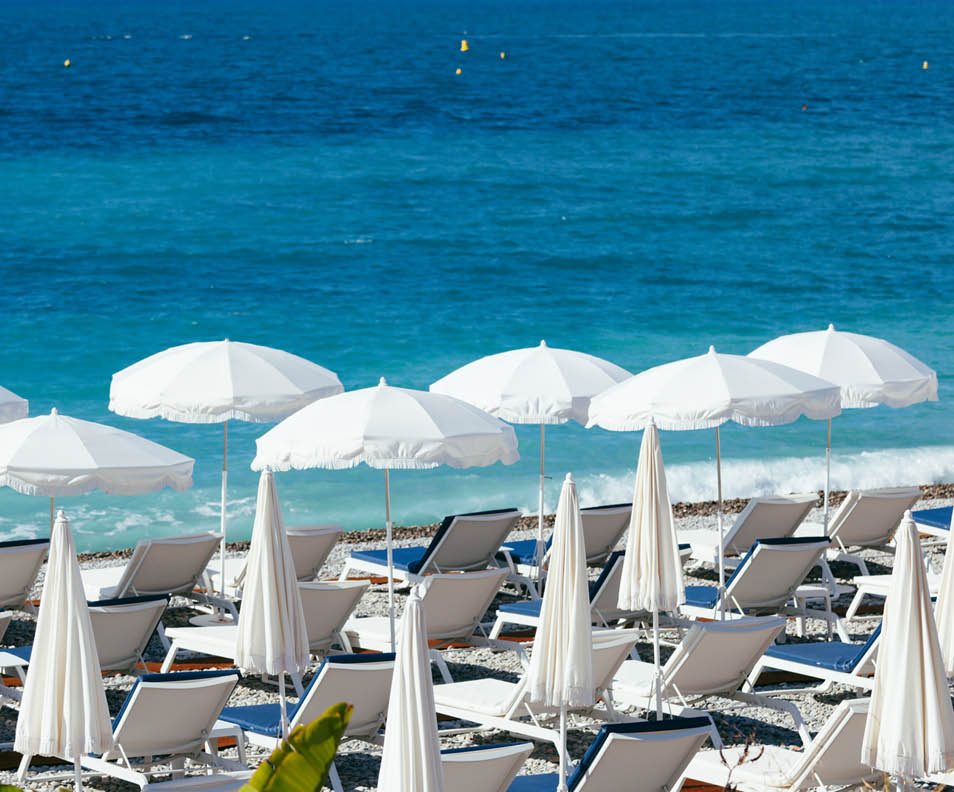 White umbrellas near turquoise Mediterranean sea on a beach of Nice, France, in early morning