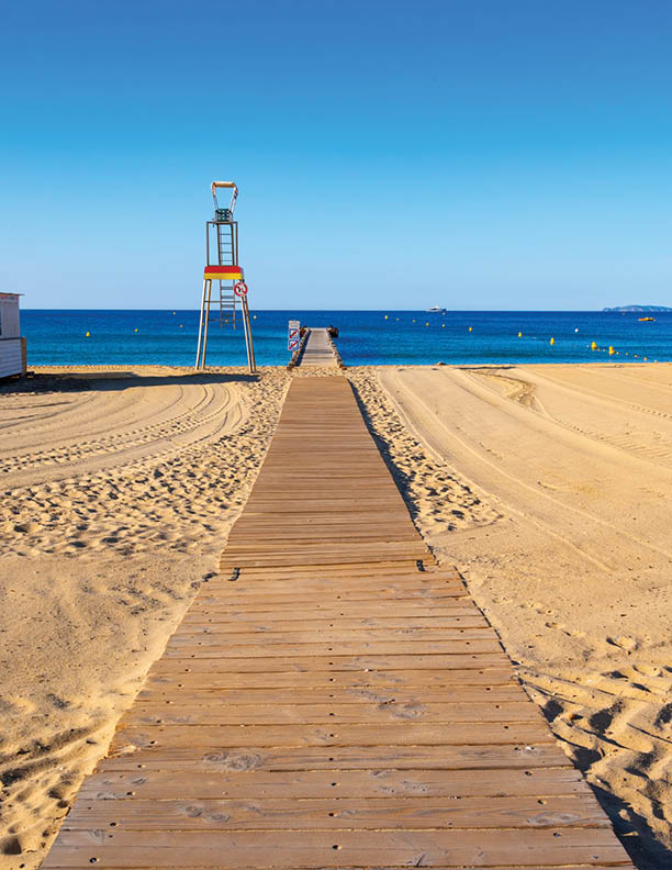 Morning view on crystal clear blue water and pier of Plage du Debarquement white sandy beach near Cavalaire-sur-Mer and La Croix-Valmer, summer vacation on French Riviera, Var, France