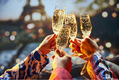 Bachelorette party. Close up shot of female hands holds glasses of sparkle wine in front of the main attraction in France. Travelling and relax. Concept of friendship, party, date, romantic, vacation.