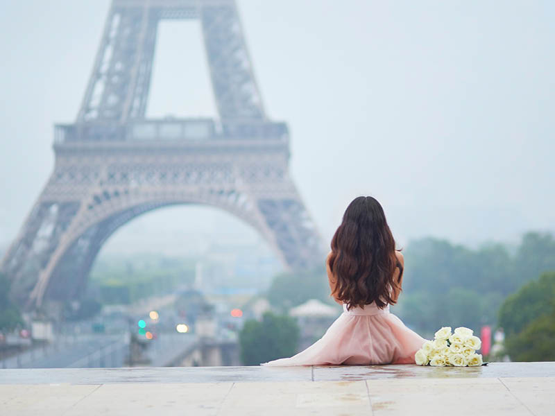 Elegant Parisian woman in pink tutu dress with white roses sitting near the Eiffel tower at Trocadero view point in Paris, France, back view
