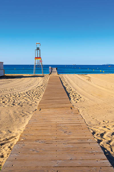 Morning view on crystal clear blue water and pier of Plage du Debarquement white sandy beach near Cavalaire-sur-Mer and La Croix-Valmer, summer vacation on French Riviera, Var, France
