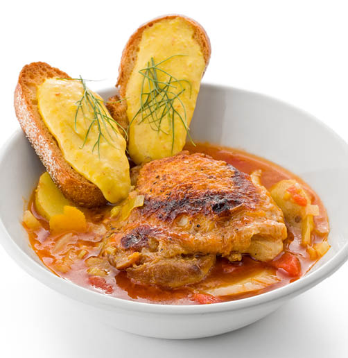 Chicken bouillabaisse in a white bowl with two slices of toast topped with rouille garnished with fennel fronds.