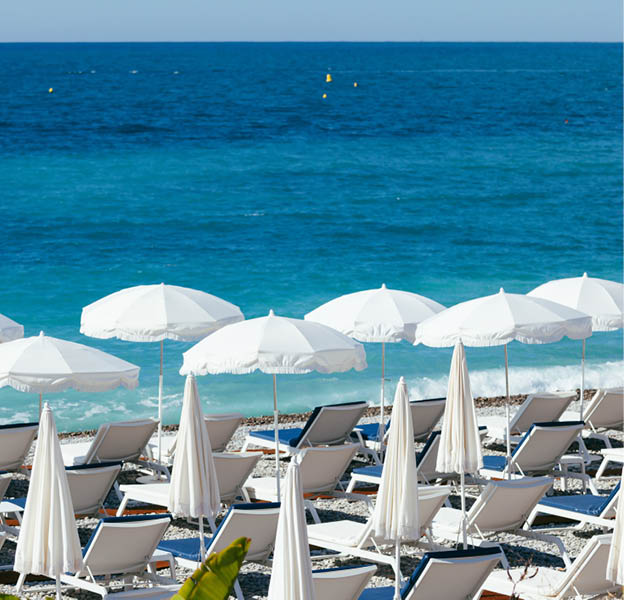 White umbrellas near turquoise Mediterranean sea on a beach of Nice, France, in early morning