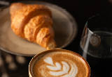 Cup of Cappuccino with beautiful cream latte art and a croissant on the side on a coffee shop table. Side view. Black Background.