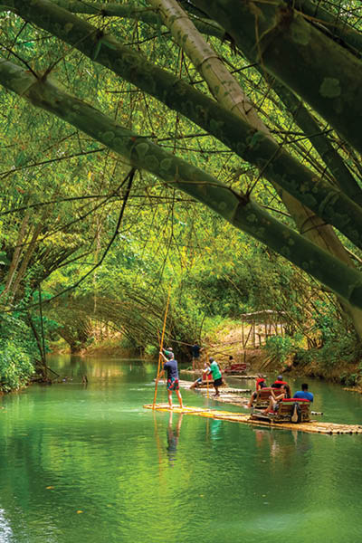 Falmouth, Jamaica - July 07 2019: Martha Brae River, Jamaica. Tourists on bamboo raft rides. Relaxing scenic tour in countryside landscape under canopy trees. People enjoy summer vacation activity.