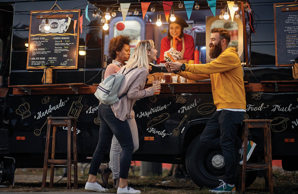 group of multiethnic young people having fun while eating in front of modified truck for mobile fast food service