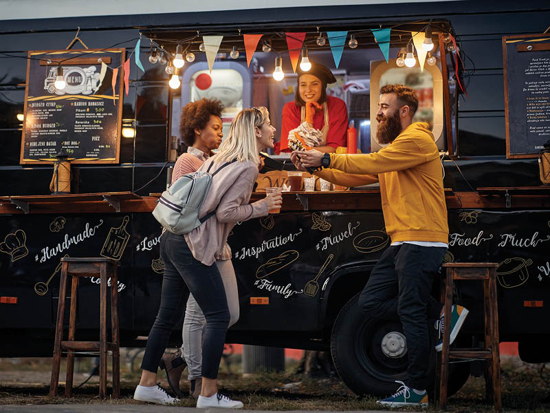 group of multiethnic young people having fun while eating in front of modified truck for mobile fast food service