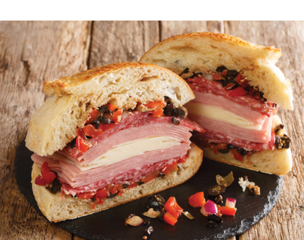 New Orleans Muffuletta Sandwich a monster of a sandwich piled high with multiple types of meat and cheese, and a perky olive salad close up on a slate board on the table. Horizontal