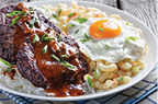 loco moco of white rice, topped with a hamburger patty, a fried egg, brown gravy, and macaroni salad served on a white plate on a rustic wooden table, Hawaiian cuisine, view from above, 