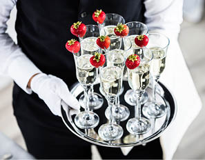 Waiter Standing With Champagne Glasses Next To Arranged Wedding Table