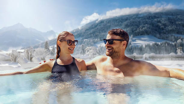 happy couple relaxing in outdoor hot tub at ski spa resort. winter vacation