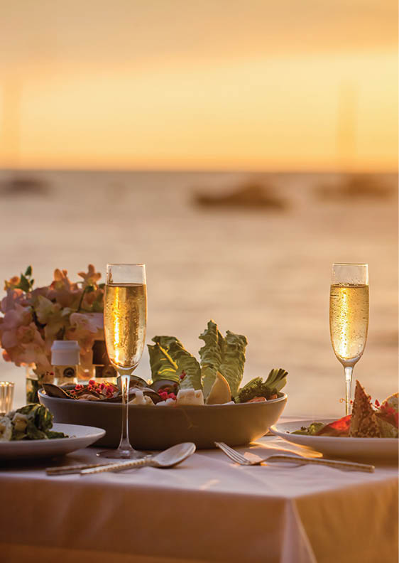 Romantic sunset dinner on the beach. Table honeymoon set for two with luxurious food, glasses of champagne drinks in a restaurant with sea view. Summer love, romance date on vacation concept.