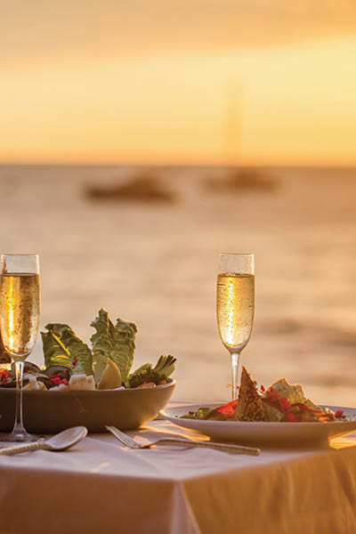 Romantic sunset dinner on the beach. Table honeymoon set for two with luxurious food, glasses of champagne drinks in a restaurant with sea view. Summer love, romance date on vacation concept.